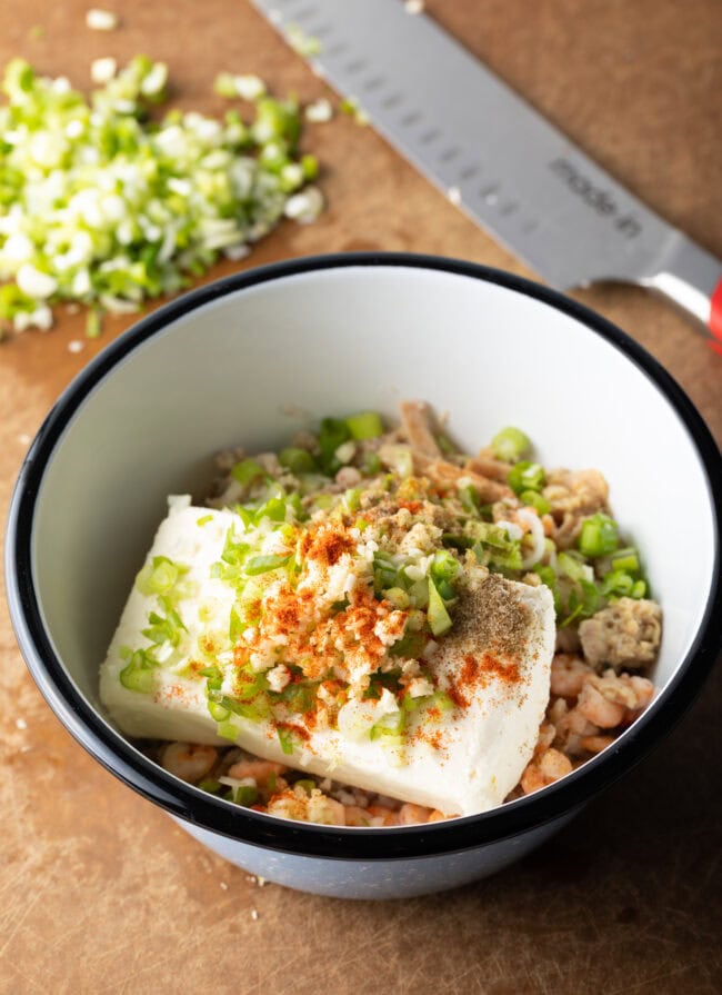 A medley of chopped seafood, herbs, and cream cheese in a white bowl.