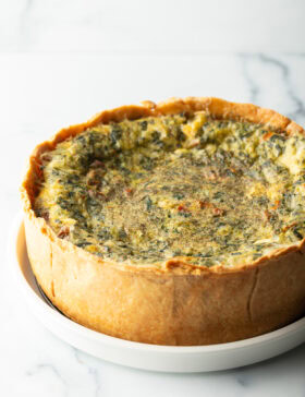 Baked veggie quiche with a deep dish crush on a white round plate.