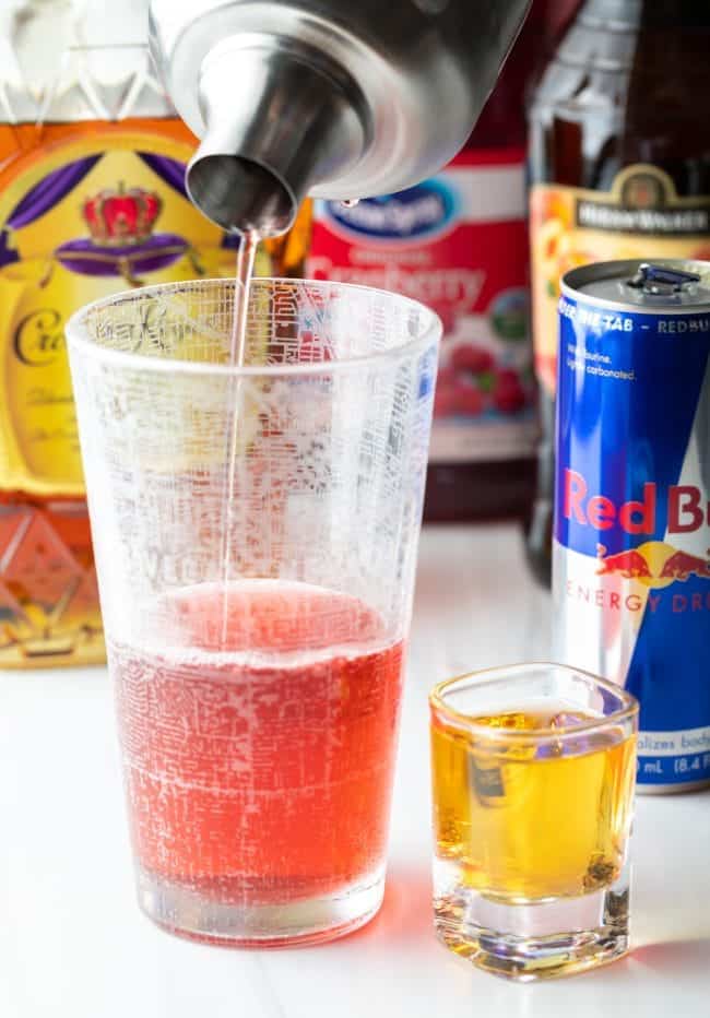 Shaker pouring Vegas bomb shot base into a tall glass with a shot of red bull on the side.
