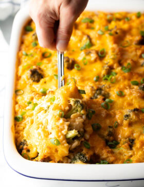 Broccoli cheese rice casserole in a white baking dish. A metal spoon is scooping a portion from the dish.