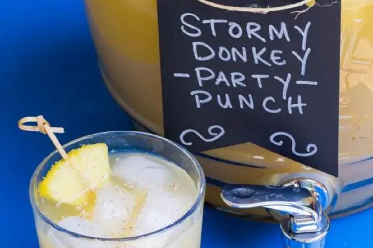 Stormy Donkey Party Punch in a drink dispenser with a glass next to it. 