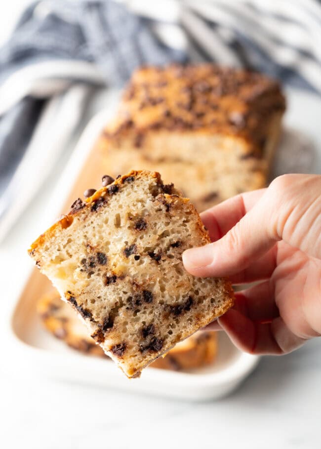 Hand holding a slice of chocolate chip ice cream bread.