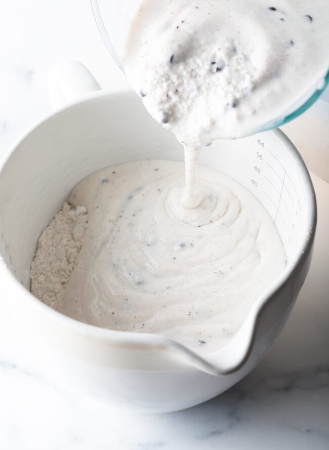 Adding melted ice cream to a white mixing bowl with flour.
