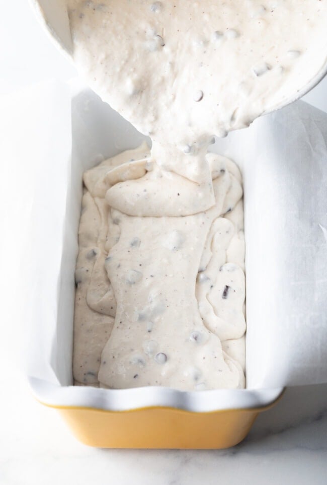 Pouring batter into a ceramic loaf pan.
