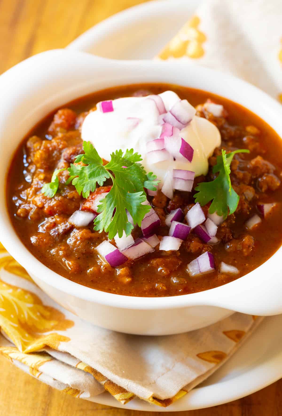 pork and pumpkin chili in a white bowl with chopped onions, cilantro, and sour cream
