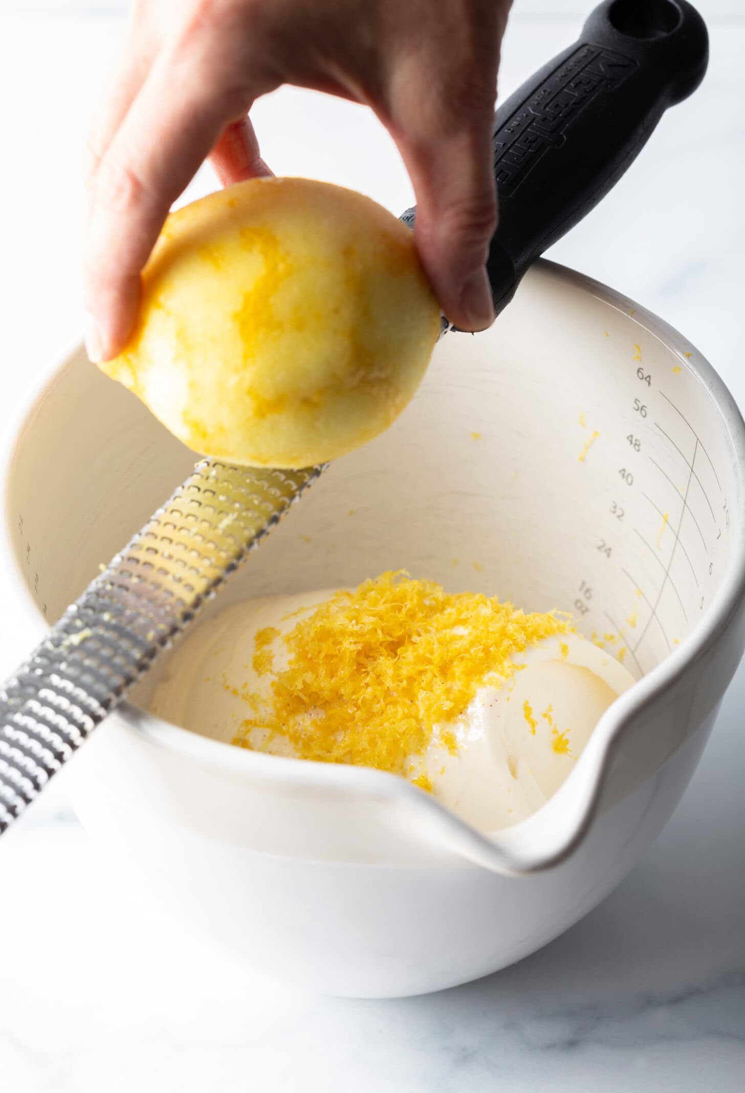 Using a zester to zest lemon into the white mixing bowl.