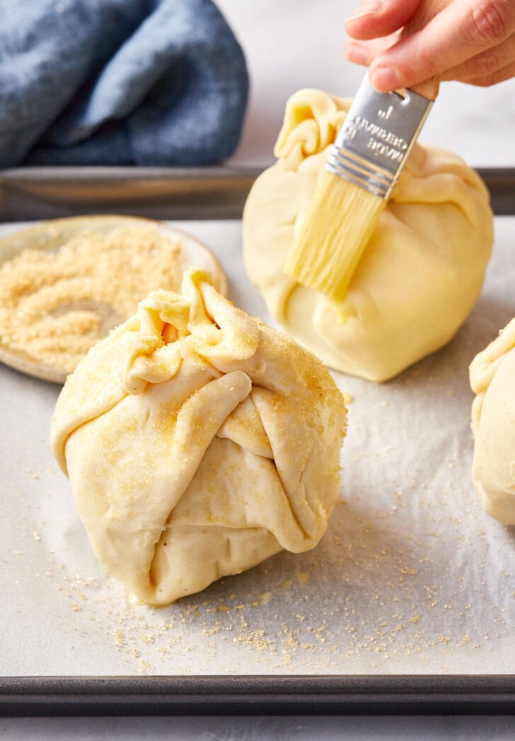 Un-baked puff pastry mini apple pie bombs with pastry brush brushing egg wash.