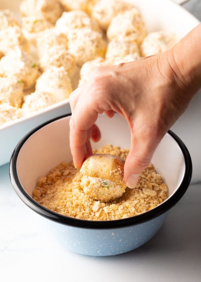 Hand rolling a stuffed mushroom in a bowl of crushed Ritz crackers.