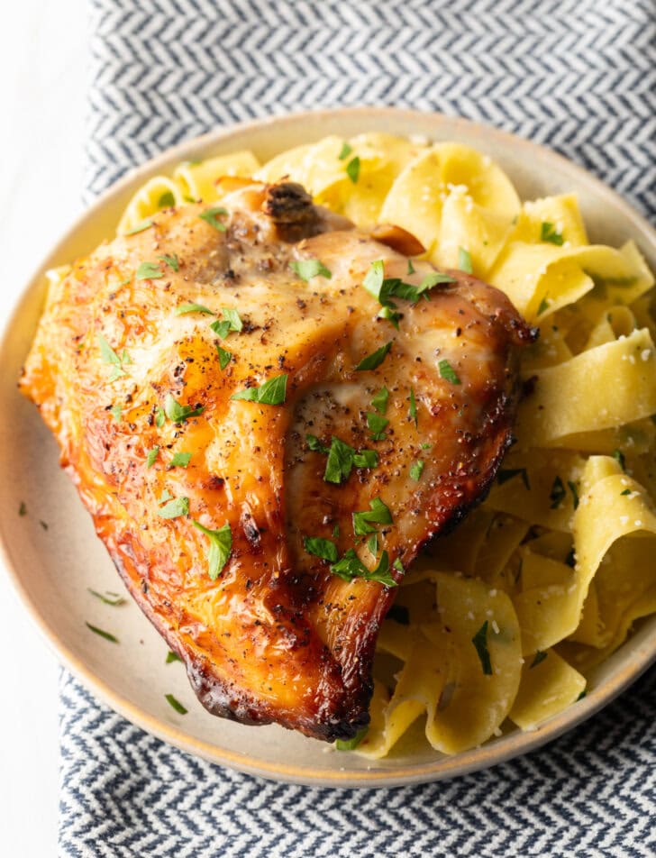 Bourbon brined chicken breast on a white plate with side of buttery noodles.