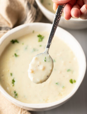 Top down view white bowl with creamy chicken soup garnished with fresh parsley. A metal spoon has a spoonful showing to camera.