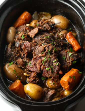 Pot roast cooked in a crock pot, with baby potatoes and large carrot chunks.