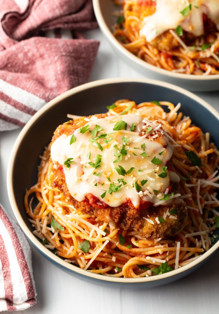 Breaded fried veal parmesan on top of spaghetti in a blue pasta bowl.
