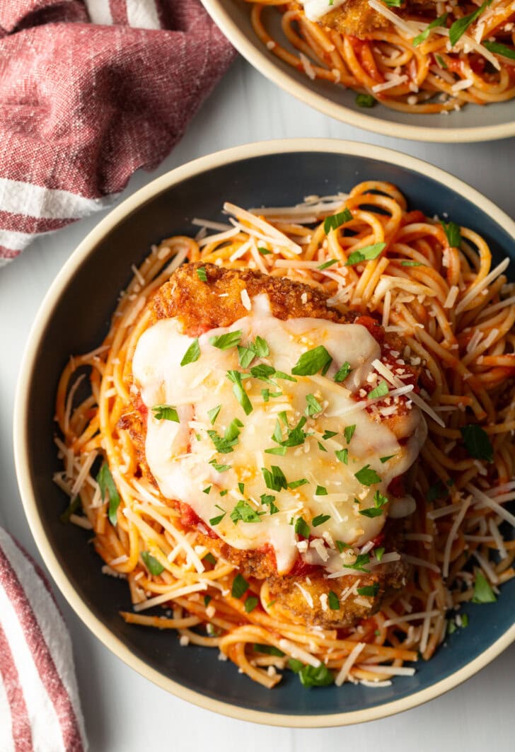Breaded fried veal parmesan on top of spaghetti in a blue pasta bowl.
