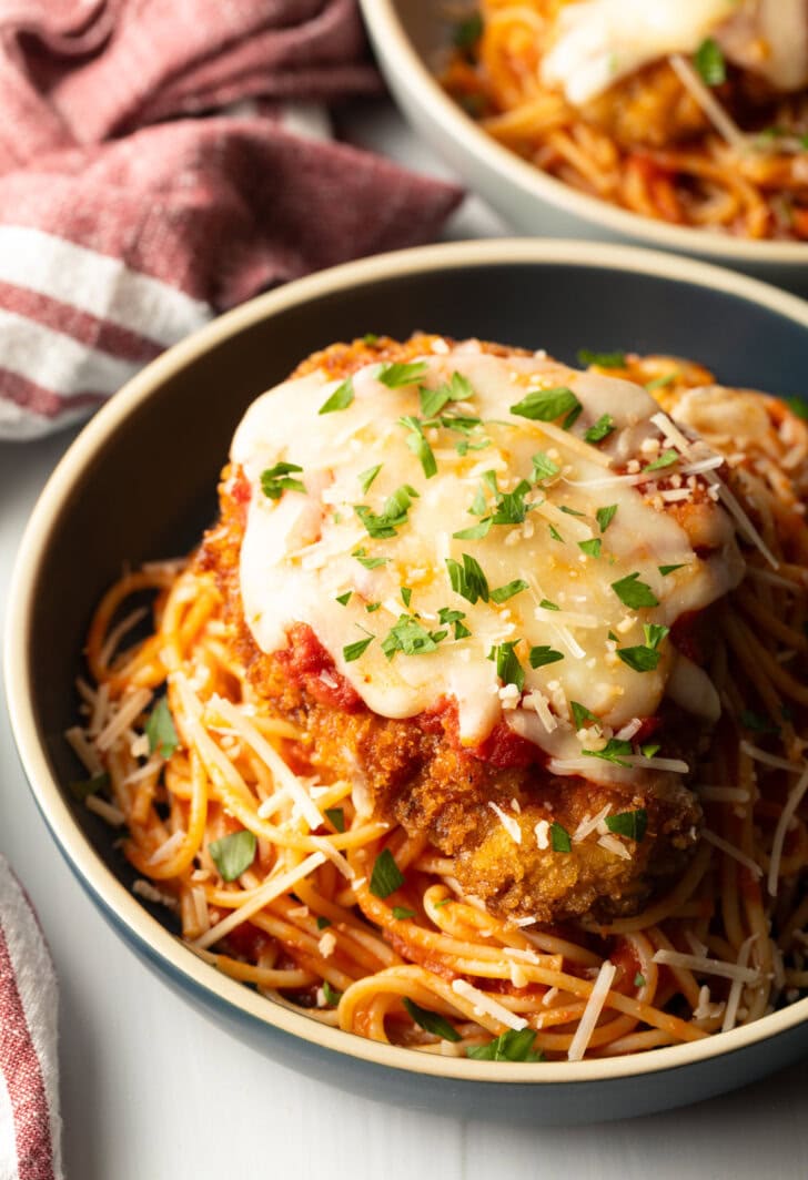 Breaded fried veal parmesan on top of spaghetti in a blue pasta bowl.