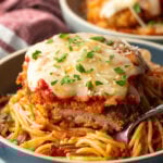 A cutlet of veal parmesan on top of spaghetti. A bite has been removed from the veal to show the juicy inside.