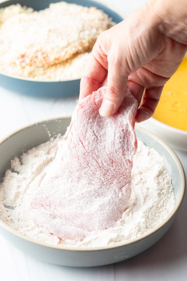 Hand dredging piece of veal in flour.