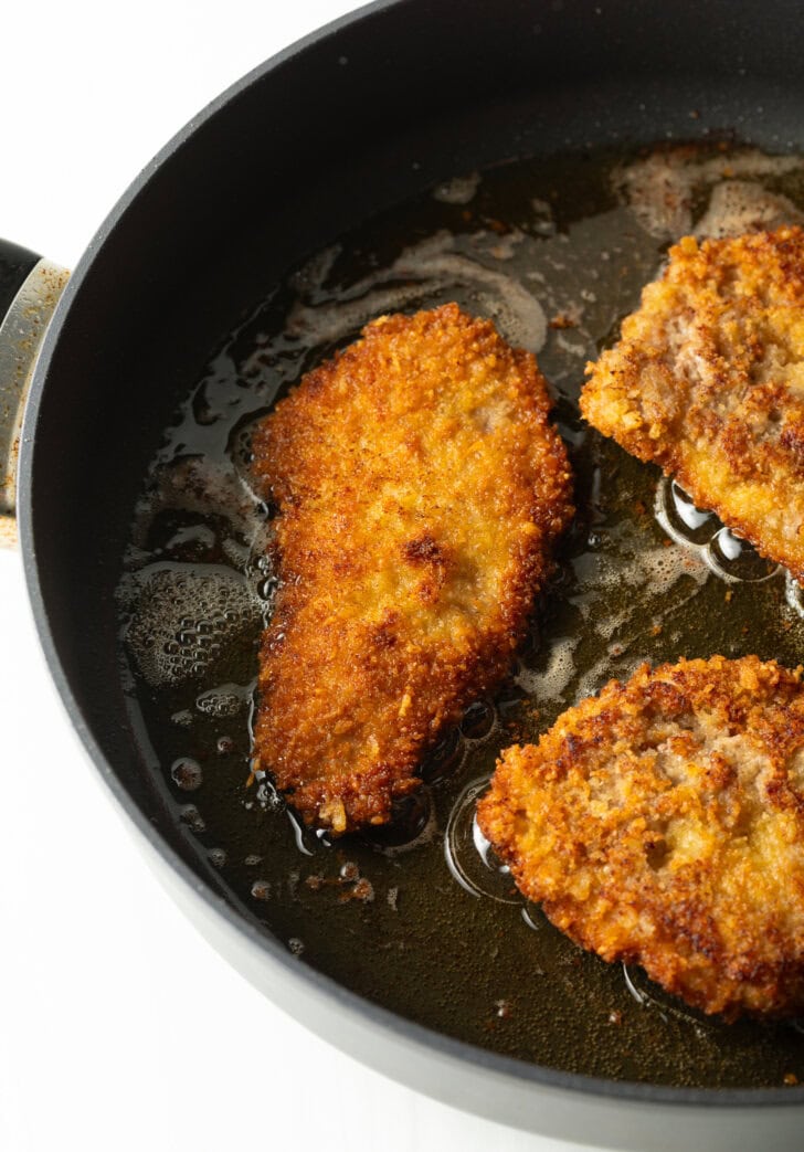 3 pieces of breaded veal cutlets, frying in a cast iron skillet.