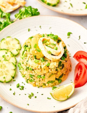 Thai fried rice recipe in a mound on a plate next to tomatoes, cucumbers and limes.