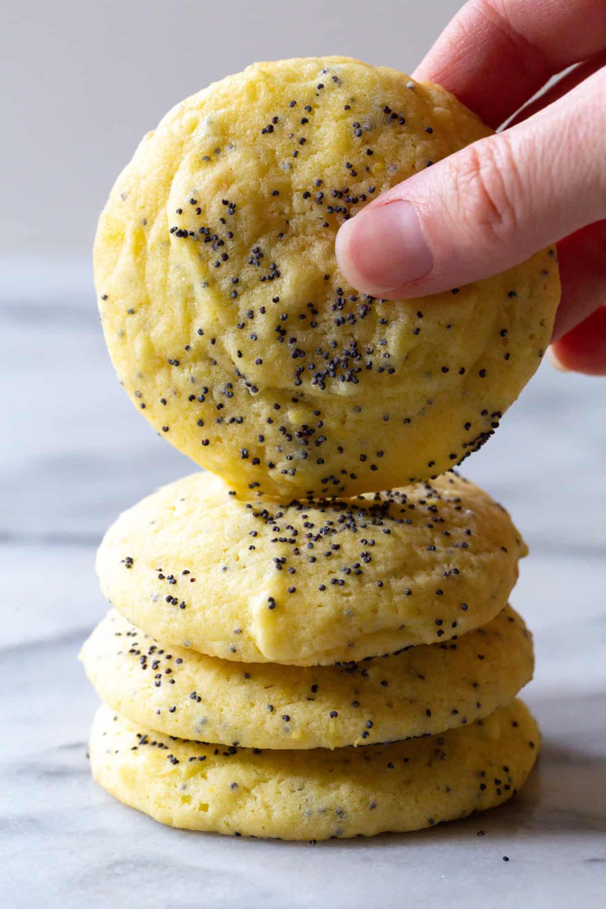Soft Lemon Poppy Seed Cookies in a stack - hand grabbing one