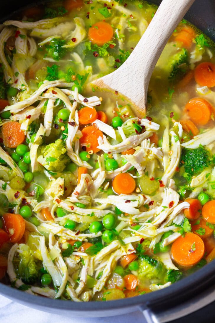 Close up shot of chicken vegetable soup in a pot with a wooden spoon. 