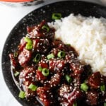 Bowl of beef teriyaki garnished with sliced green scallions, with white rice side-by-side in the bowl.