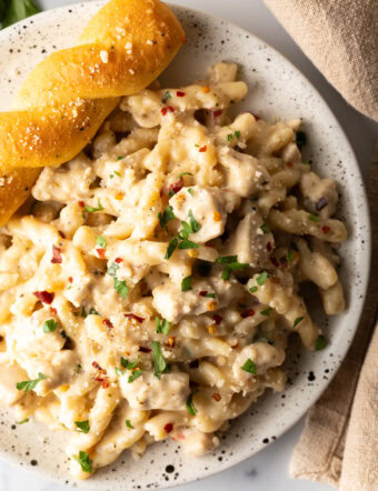 Top down view of white plate of cheesy garlic parmesan chicken pasta with a breadstick twist on the side of the plate