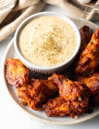 Plate of chicken wings with ramekin of garlic parmesan sauce.