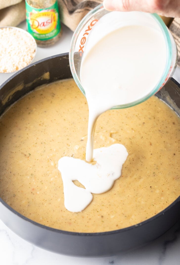 Pouring heavy cream from a glass measuring cup into a skillet of garlic sauce.