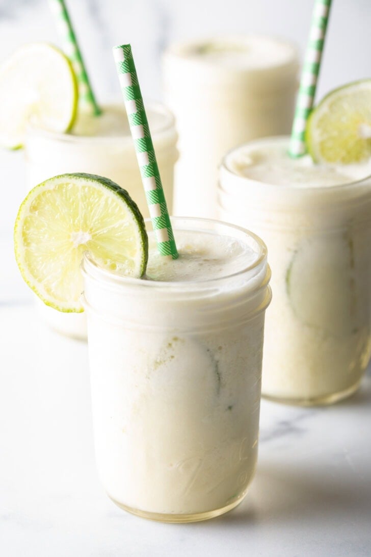 four glasses of Brazilian limeade, each garnished with a slice of lime and a green and white striped straw
