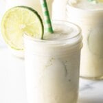Four glasses of Brazilian limeade, each garnished with a slice of lime and a green and white striped straw.