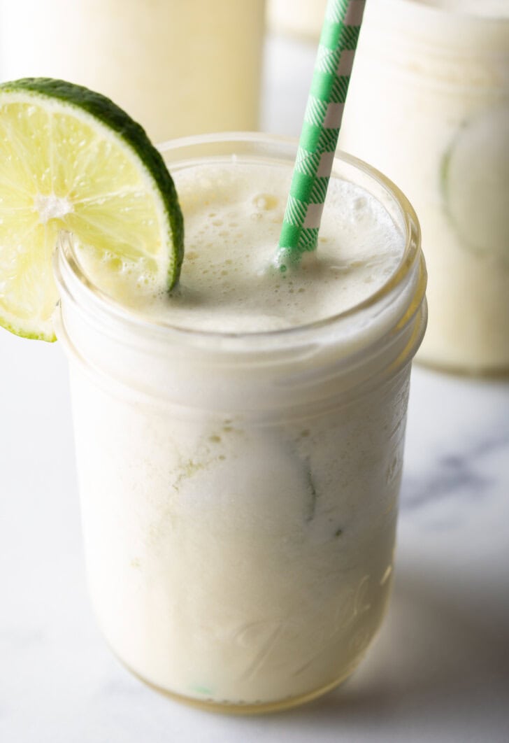 Glass of Brazilian lemonade garnished with a slice of lime and a green and white striped straw