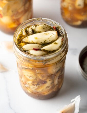 Top down open glass jar stuffed with preserved garlic and herbs.
