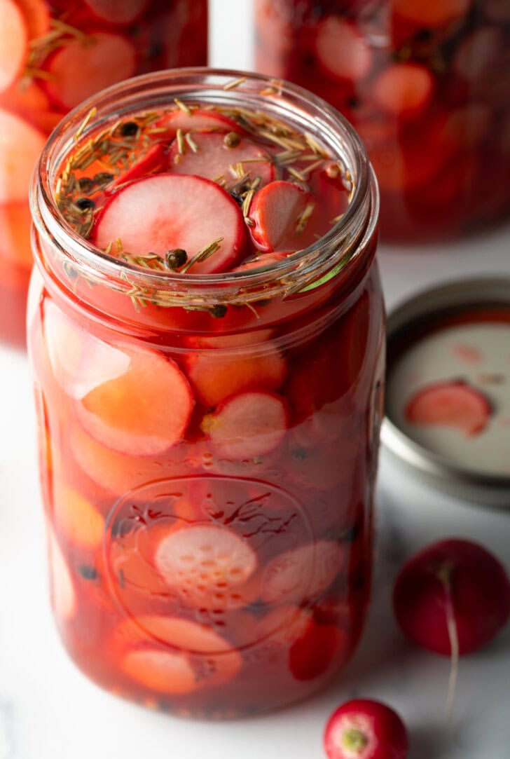 Large open glass jars of pickled radish slices.