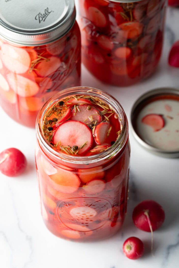 Large open glass jars of pickled radish slices.