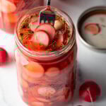 Fork picking out several pickled radishes from a large glass jar.