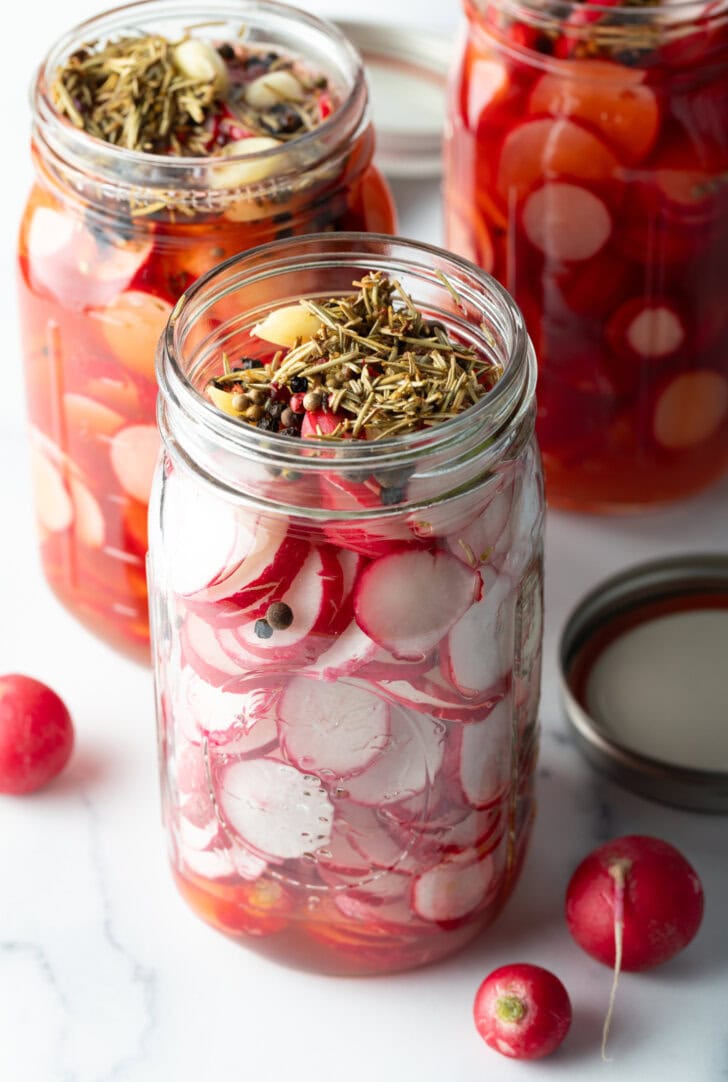 Glass jar with radish slices and aromatics.