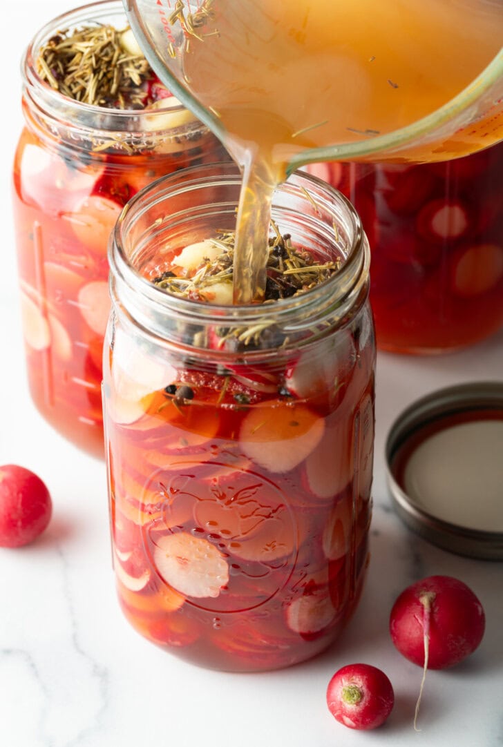 Pouring pickling liquid from a glass measuring pitcher into the glass jar of radish slices.