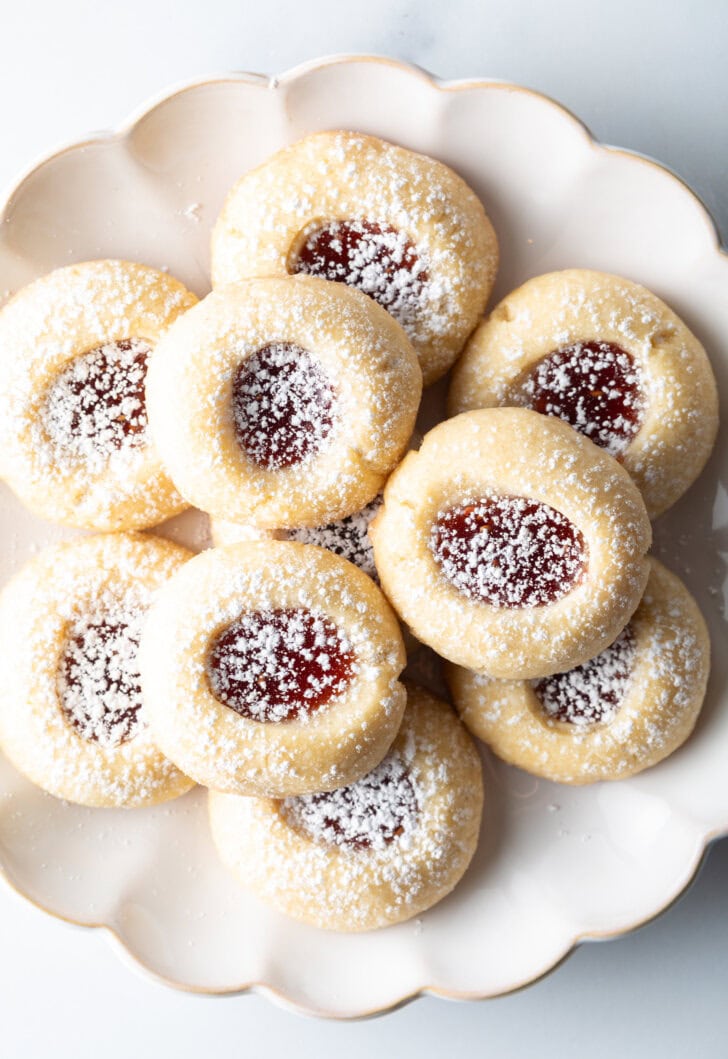 Top down view of raspberry thumbprint cookie stacked two-high on a white plate, dusted with powdered sugar.