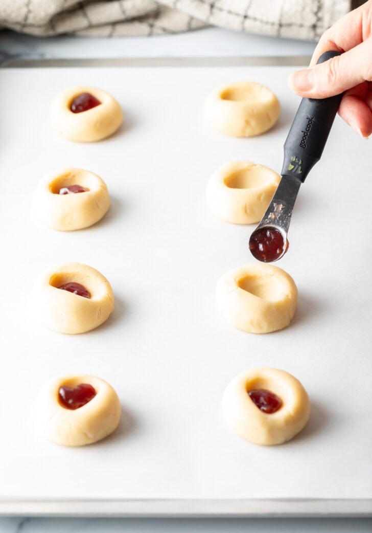 Small measuring spoon adding a bit of raspberry jam into the unbaked cookie dough.