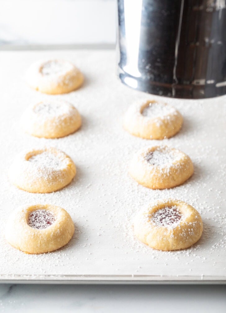 8 cookies in on a baking sheet being dusted with powdered sugar.