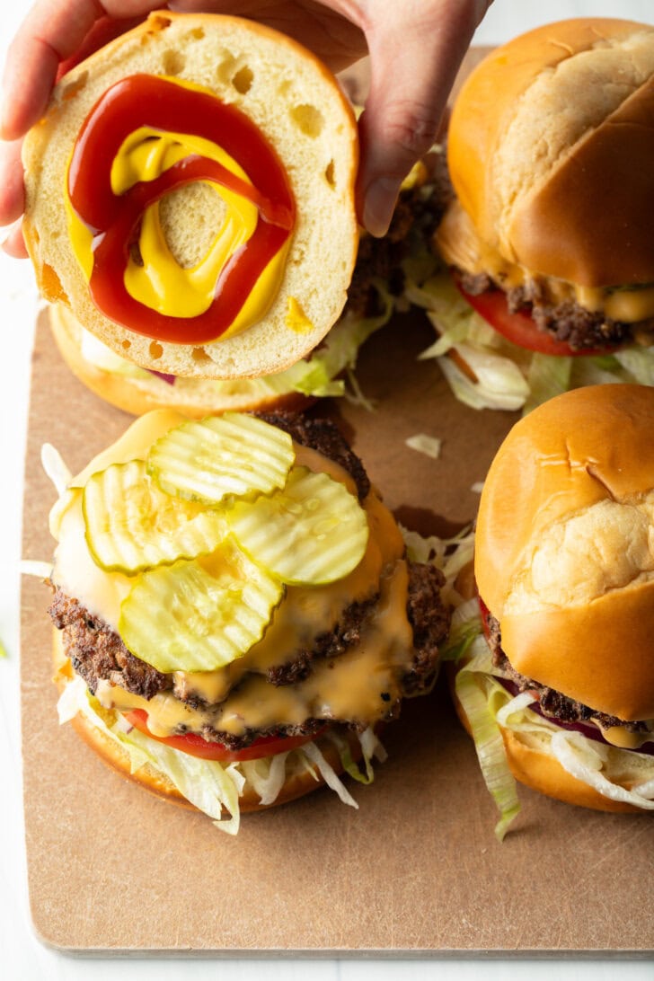 Topping hamburger with bun and pickles.