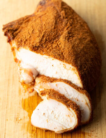 Spice-rubbed smoked turkey breast on a wood cutting board, two slices are in front of the breast.