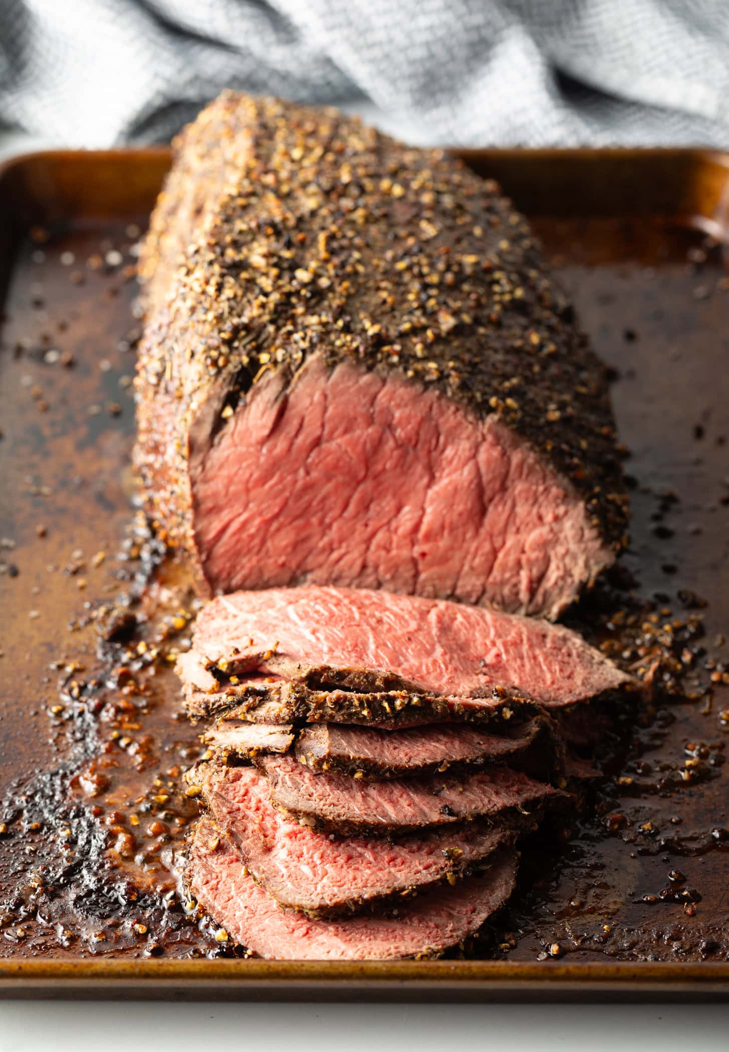 Cooked beef round roast on a metal baking pan. The front half of the roast has been thinly sliced.