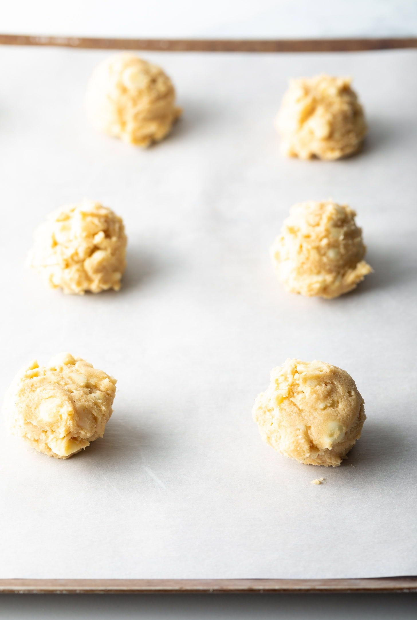 6 balls of white chocolate chip macadamia nut cookie dough on parchment paper.