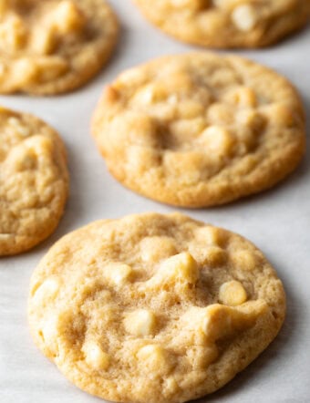 Close up view of three white chocolate macadamia nut cookies on parchment.
