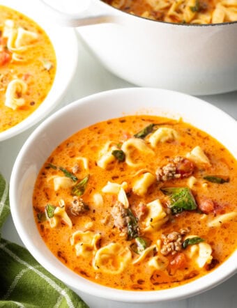 Top down view white bowl with creamy sausage and tortellini soup. The large pot of soup is off to the side.