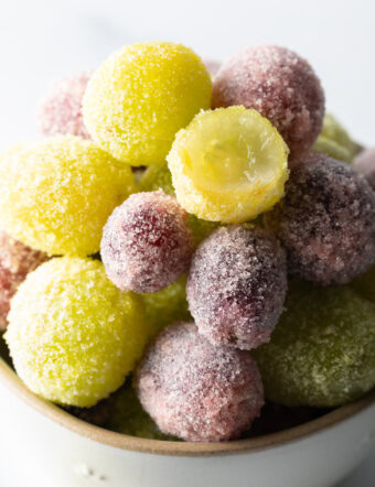 a bowl of green and purple candy grapes. One of the green grapes has been bitten in half to show the inside.