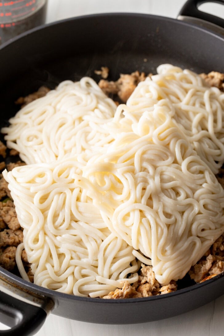 Uncooked udon noodles in a skillet.