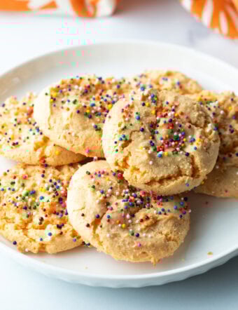 White plate with a pile of 6 cookies, all decorated with sprinkles.