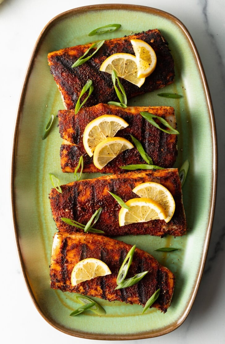 Top down view of 4 pieces of blackened and grilled fish, all topped with slices of lemon and green onions.